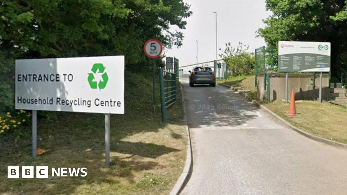The entrance to Bidston Household Waste Recycling Centre with a large hite sign that says entrance in black writing. A car is travelling along the access road. There is a red circle road sign with 5 written on in black.