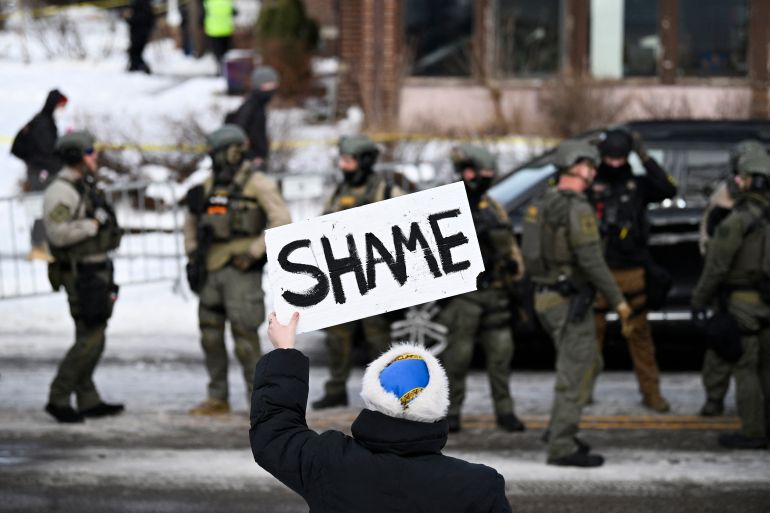 MINNEAPOLIS, MINNESOTA - JANUARY 07: An onlooker holds a sign that reads "Shame" as members of law enforcement work the scene following a suspected shooting by an ICE agent during federal law enforcement operations on January 07, 2026 in Minneapolis, Minnesota. According to federal officials, the agent, “fearing for his life” killed a woman during a confrontation in south Minneapolis. Stephen Maturen/Getty Images/AFP (Photo by Stephen Maturen / GETTY IMAGES NORTH AMERICA / Getty Images via AFP)