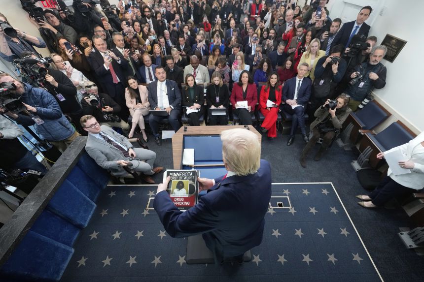 President Donald Trump holds a stack of images of people he said were apprehended in Minnesota as he arrives for a press briefing at the White House in Washington, DC, on  Tuesday.