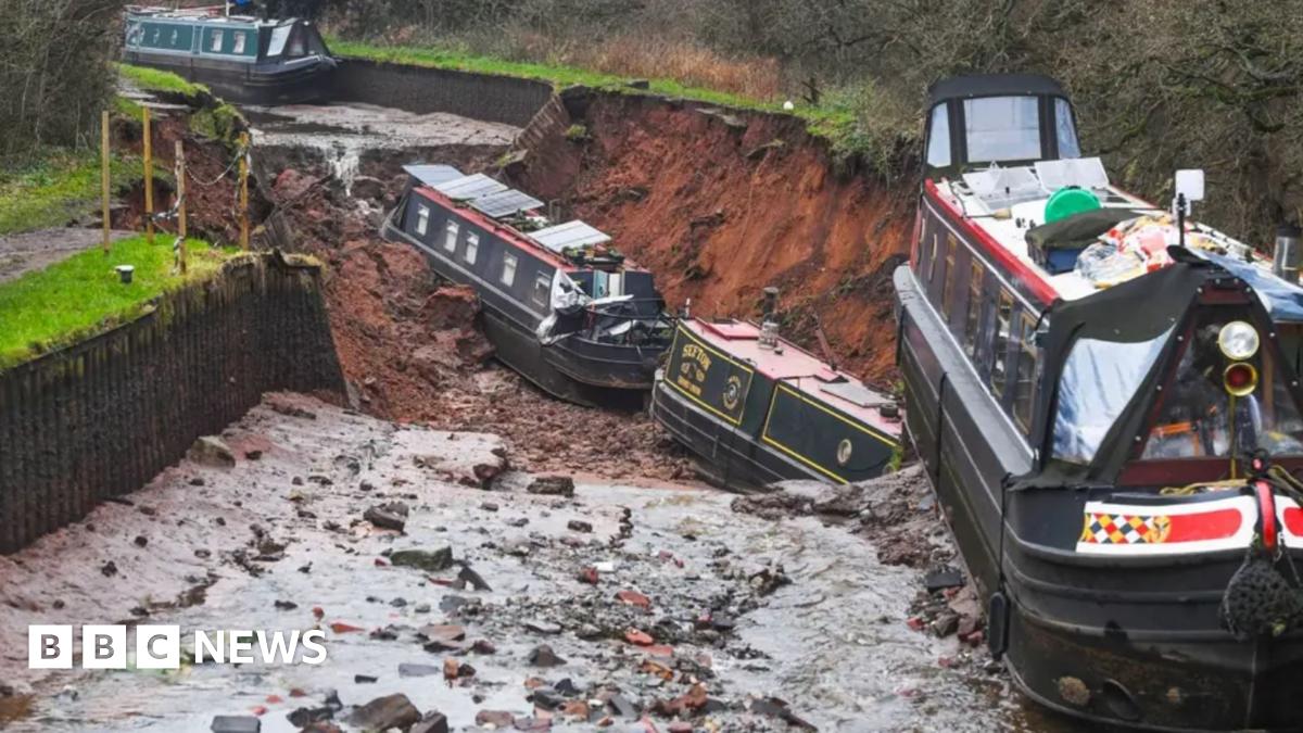Three boats in a dry but muddy canal with two at the bottom of a deep hole