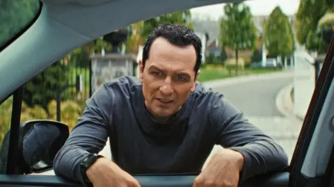 The Beast In Me / Netflix Matthew Rhys as Nile Jarvis in The Beast In Me peers through car window with a grimace