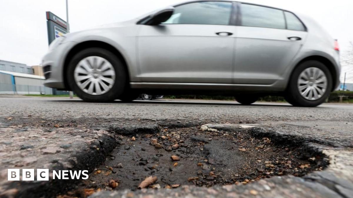 Grey car drives past pothole on a road