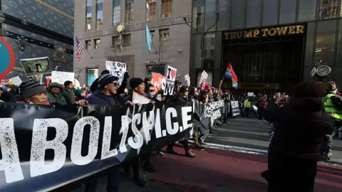 AFP via Getty Images People hold signs outside the Trump tower as they participate in a protest organized by Rise and Resist against US Immigration and Customs Enforcement (ICE) activities and the US intervention in Venezuela in New York on January 11, 2026