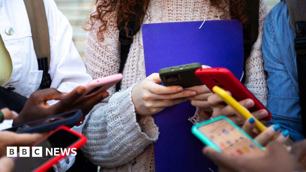 Six young people standing in a group holding smartphones of different colours.