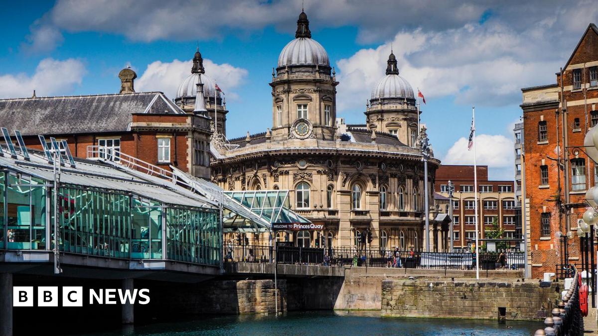 A waterfront scene with a glass walkway on the left and buildings in the distance.