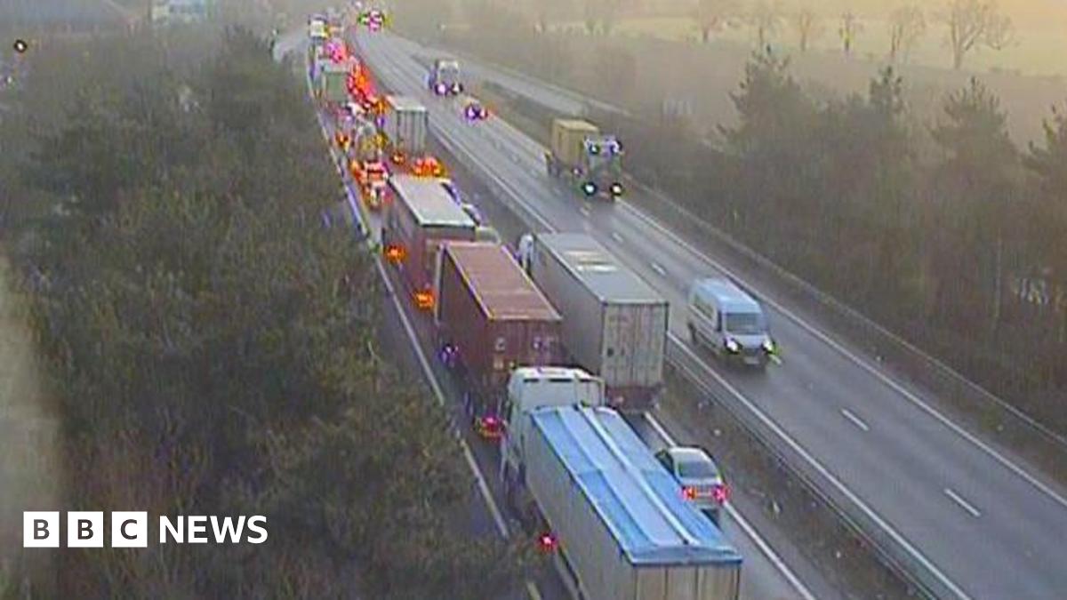 Millie Bobby Brown and David Harbour in character as Eleven and Jim Hopper. Eleven wears red shorts over grey leggings and a grey jumper. Jim Hopper wears a black leather jacket, a black beanie hat and dark trousers.They are speaking to director Frank Darabont on the set of Stranger Things. There is a vintage advertisement posted in the background with debrief on the ground.