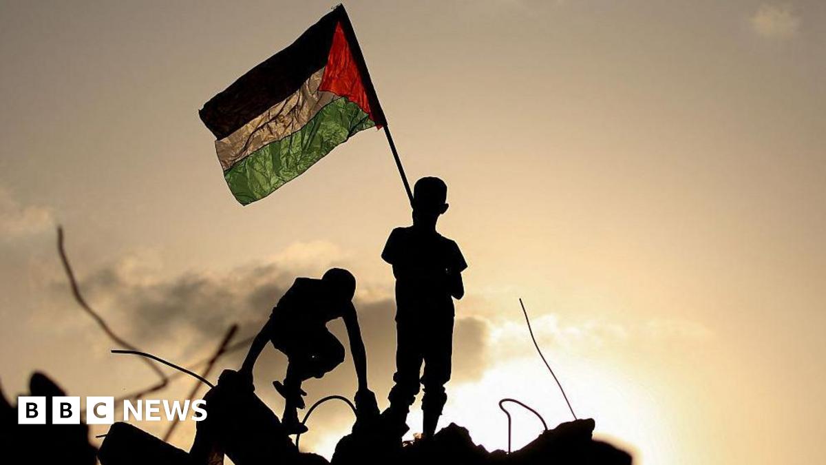 Palestinian children play as one waves a Palestinian national flag as he stands on the rubble of a destroyed building at the Bureij camp in Gaza. They are silhouetted against a setting sun illuminates the background of the image.