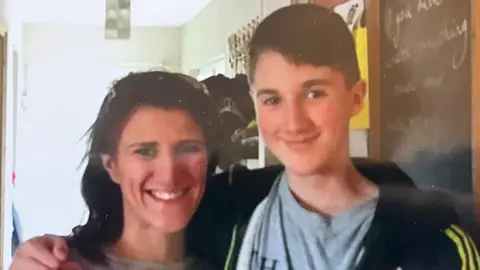 Kate Roux Kate Roux and her son Ben smile at the camera with arms wrapped around each other. She is shorter, with long brown hair. He has short brown hair, dimples and brown eyes. He's wearing a hoody with yellow stripes at the shoulder and a grey t-shirt. 