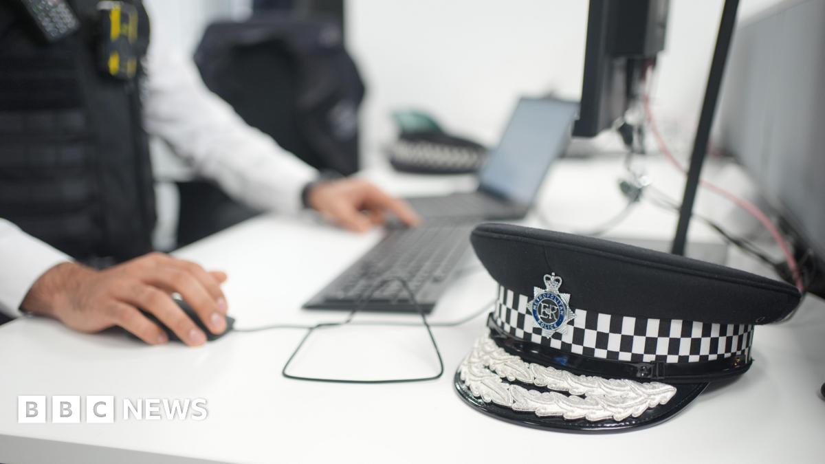 Police hat in foreground next an officer using to keyboard, laptop and computer screen in background
