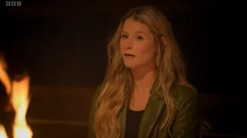 Mollie looking upset, lit by the fmales of a fire, in the Traitors series two final