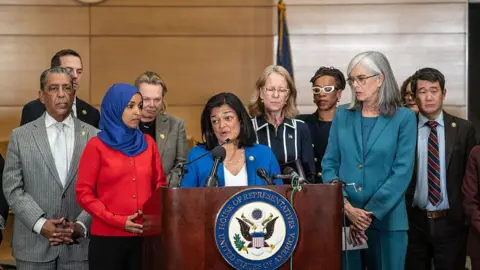 Bloomberg via Getty Images lawmakers stand in front of podium with Rep. Pramila Jayapal speaking into a microphone