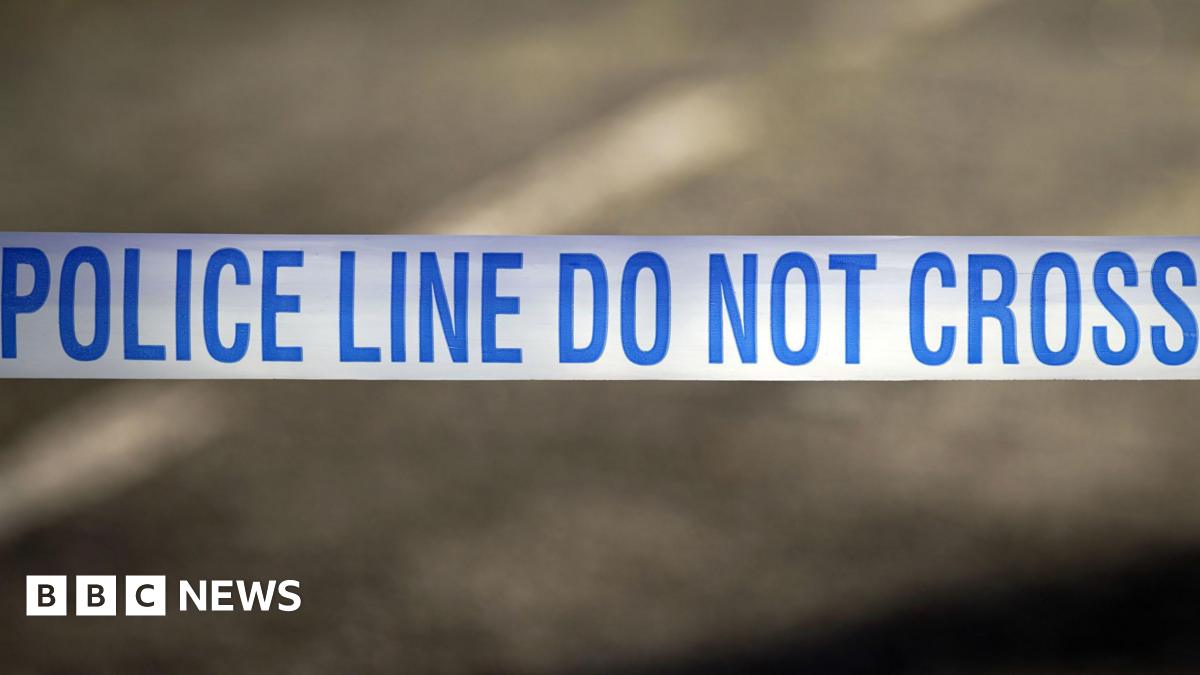 A blue and white line of tape is stretched across a road. it has the words police line do not cross om it in blue.