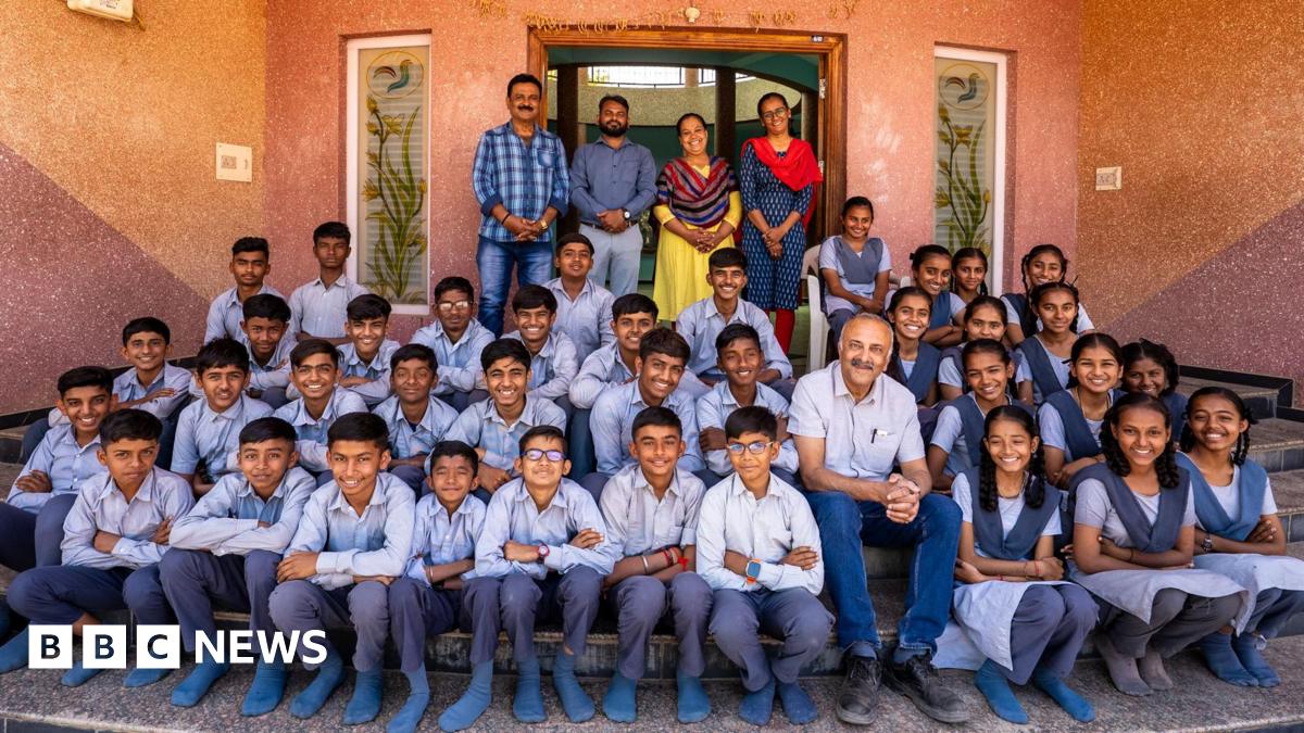 Bhasker is sitting with a class of girls and boys in their blue school uniform