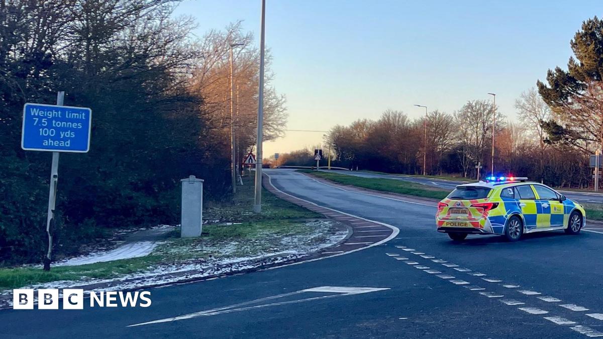 The A120 road which runs through Essex. On the carriageway there is a parked yellow and blue fluorescent marked police car which is blocking the way for any traffic to get down the road. On the right of the picture is a green sign pointing people to Stansted and Braintree.