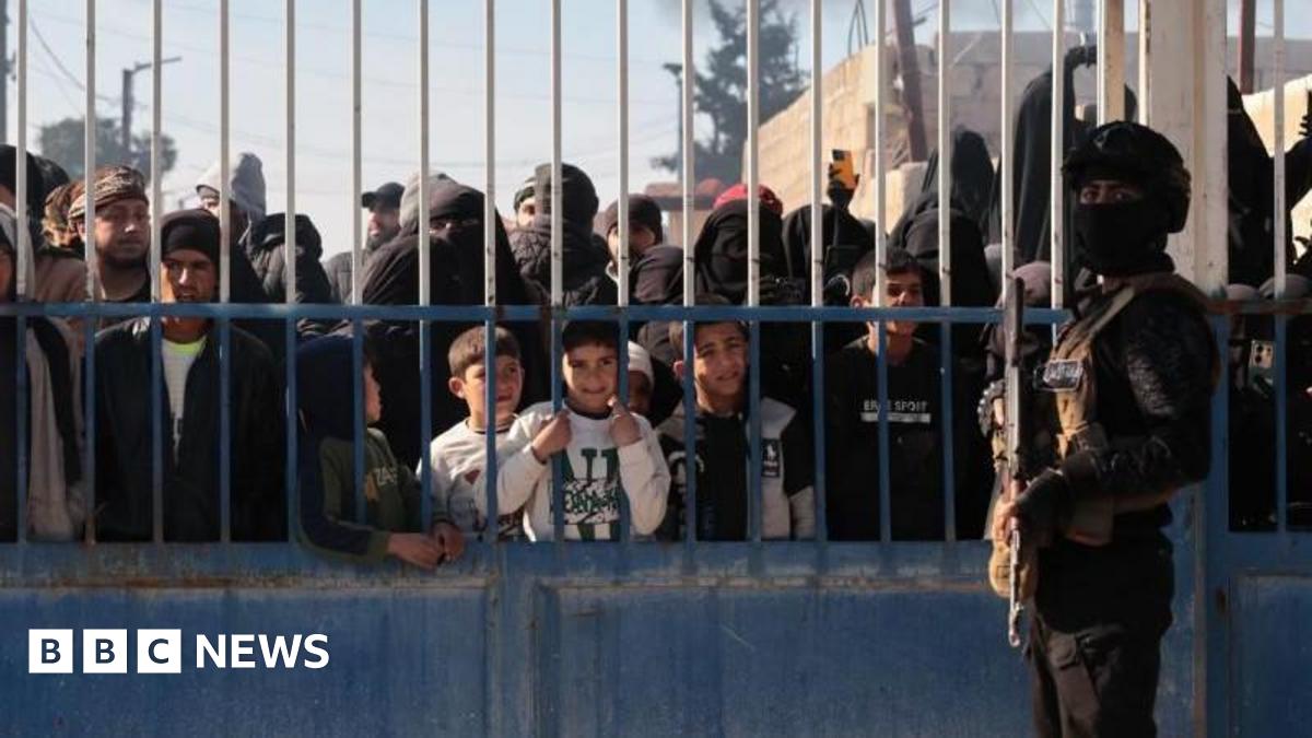 man stands in front of gate with prisoners behind