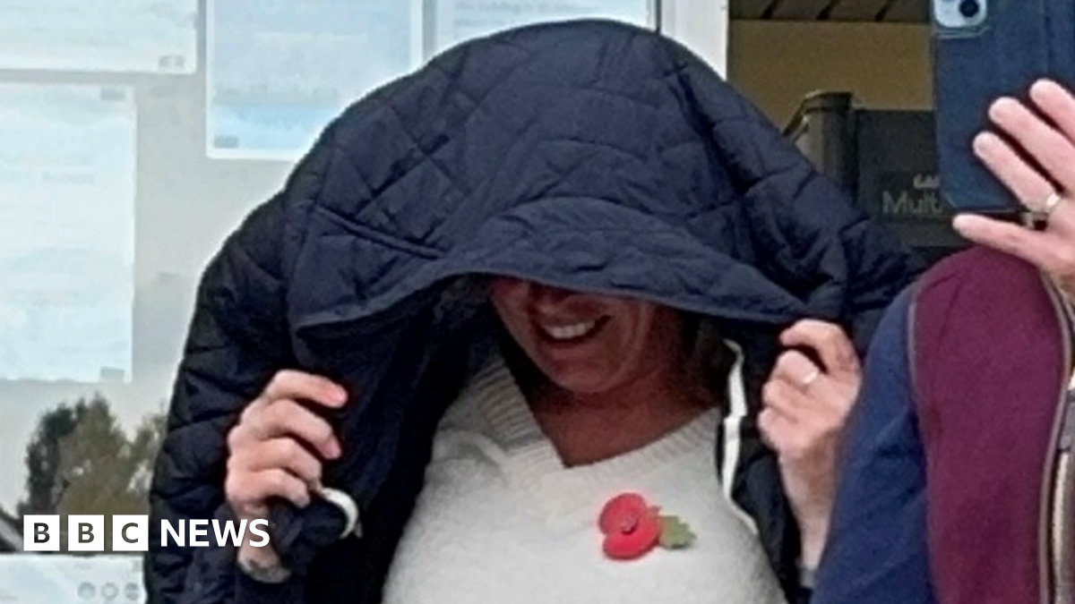 A close-up photo of Rebecca Pinckard walking out of court with her black coat over her head as she tries to cover her face. She appears to be smiling under the coat. She is wearing a cream jumper with a poppy on it.