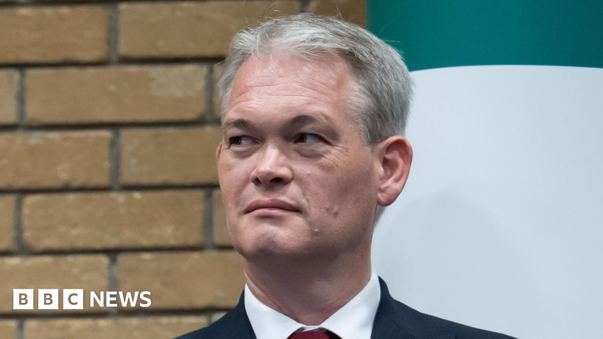 Two men - one smiling with a green Plaid Cymru badge and one not smiling with a red Labour badge - stand on a stage next to each other.