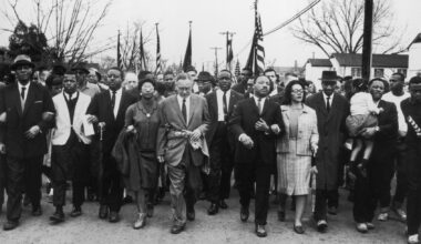 March 1965:  American civil rights campaigner Martin Luther King (1929  - 1968) and his wife Coretta Scott King lead a black voting rights march from Selma, Alabama, to the state capital in Montgomery;  among those pictured are, front row, politician and civil rights activist John Lewis (1940 – 2020), Reverend Ralph Abernathy (1926 - 1990), Ruth Harris Bunche (1906 - 1988), Nobel Prize-winning political scientist and diplomat Ralph Bunche (1904 - 1971), activist Hosea Williams (1926 – 2000 right carrying child). (Photo by William Lovelace/Daily Express/Hulton Archive/Getty Images)