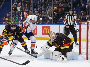 Kevin Lankinen (32) makes the save as teammate Filip Hronek (17) ties up New York Islanders' Anders Lee (27) during the first period