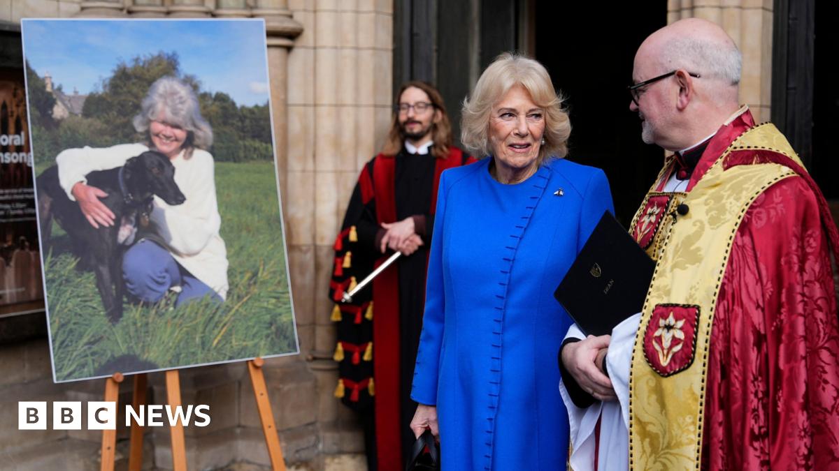 The Queen speaks to the Dean while both stand next to a printed image of Jilly Cooper