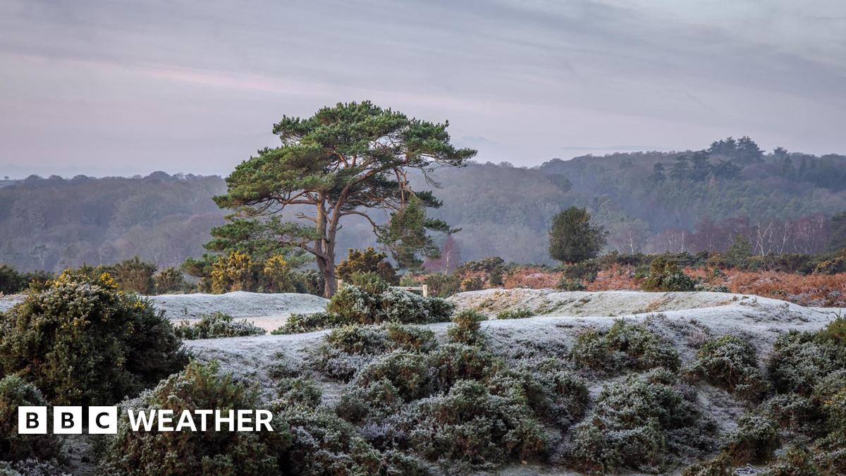 A young boy and girl, wearing blue and pink clothes, patting down snow on a snowman bigger than them