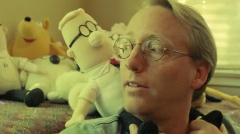 Getty Images Scott Adams pictured in front of a stuffed toy doll of his character Dilbert