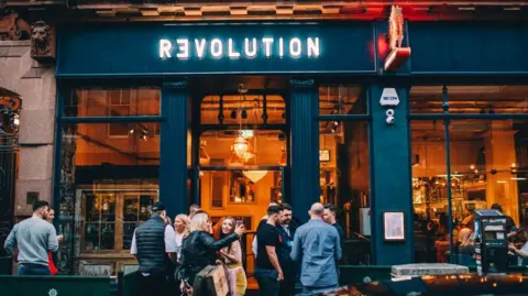 Revel Collective A Revolution branded bar with revellers gathered outside.