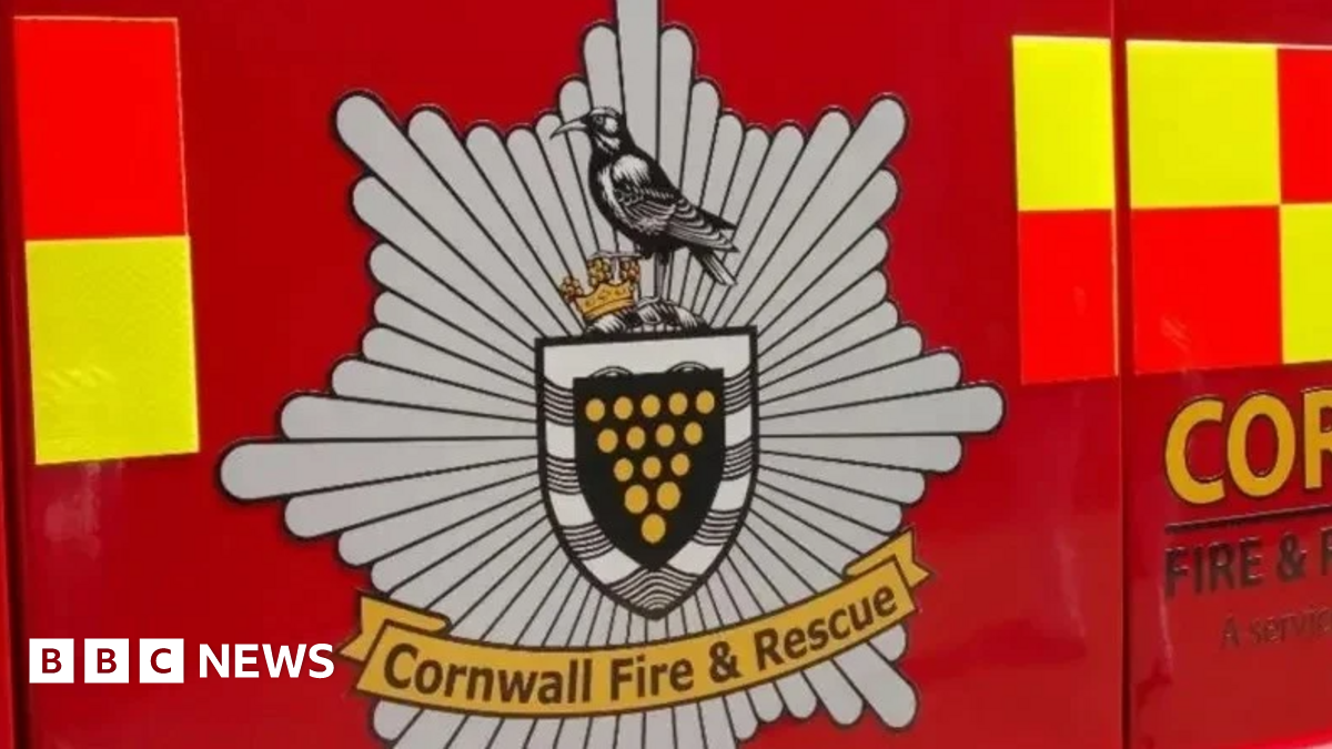 A close-up of the side of a red fire truck, showing the Cornwall Fire & Rescue logo. The logo features a chough, a small black bird.