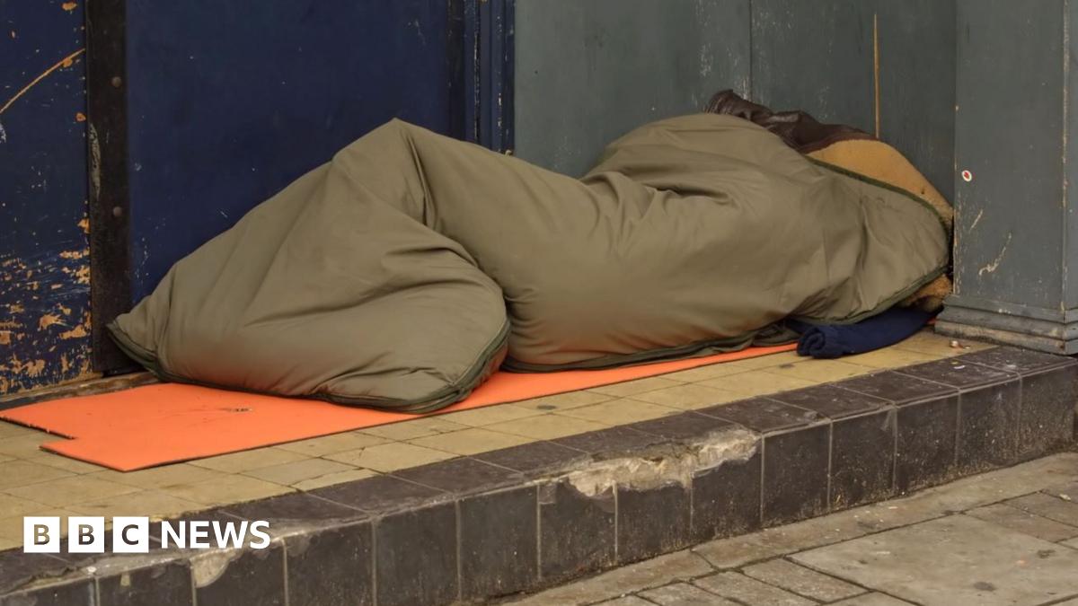A figure in a brown sleeping back on a tiled step