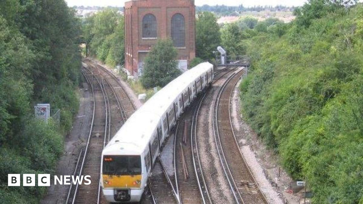 A train is on the track at Dartford Junction, crossing from one side to the other. There is a building where the junction divides into two routes. Trees line the junction on either side.