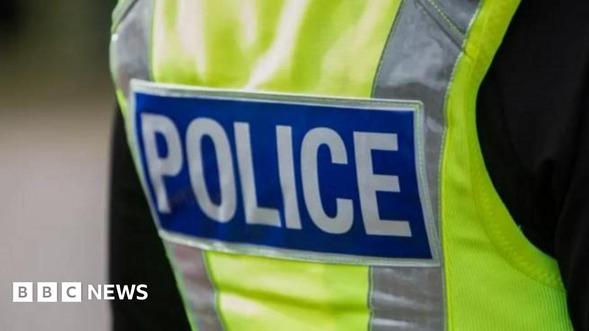 The back of a police officer wearing a hi-vis gilet and black top. In the centre of the gilet is the word Police in white capital letters on a blue background.