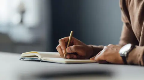 Getty Images A man writing in a notebook. 