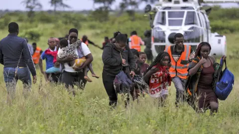 EPA/Shutterstock A group of people, including people holding children, leave a white helicopter that has landed in a field in Mozambique.