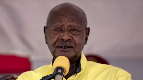AFP via Getty Images Museveni speaks into a yellow microphone, wearing a similarly coloured yellow shirt