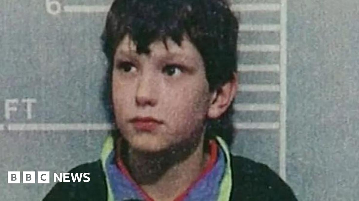 A police custody shot of a young Jon Venables, wearing a dark jumper, after his arrest. He is standing in front of a height chart showing he stands just over 4ft 6in tall.