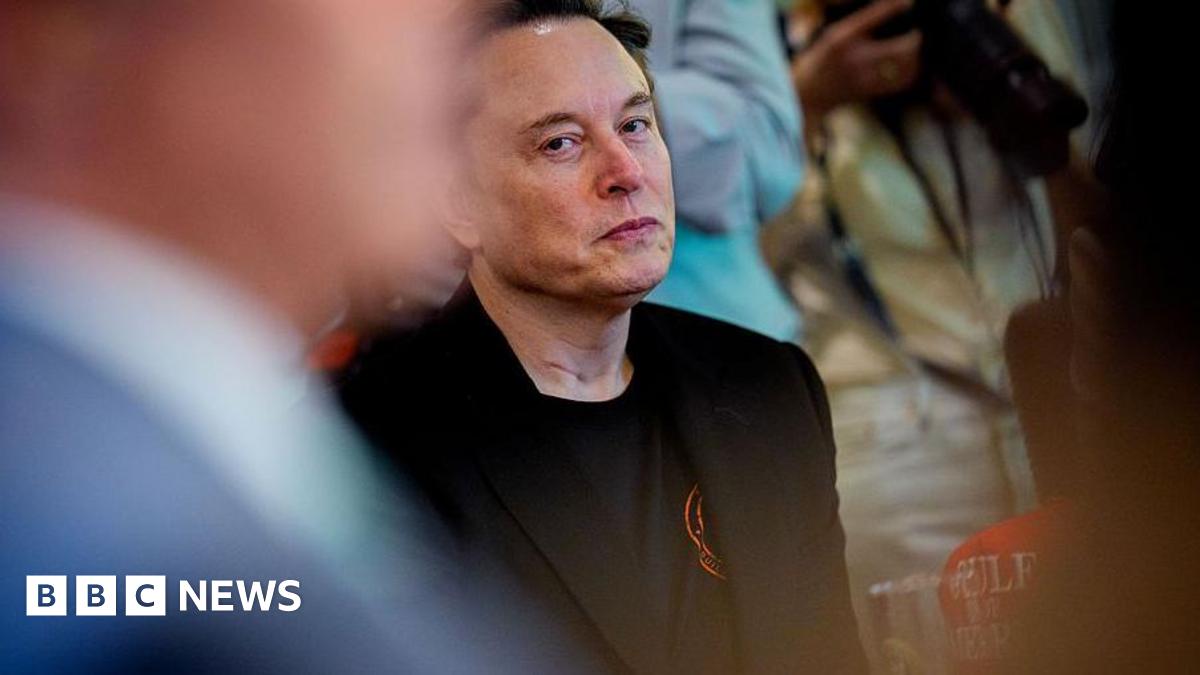 Donald Trump and Keir Starmer sit in a formal drawing room setting  on arm chairs with US and UK  flags behind them. Both have serious expressions and are looking out and not at each other.