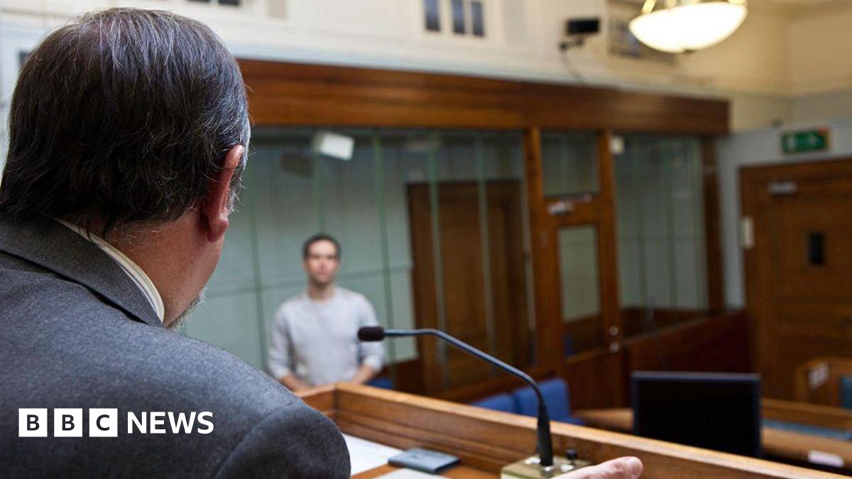 Rear view of male magistrate with dark hair addressing a young man in the dock