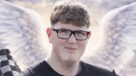 South Yorkshire Police An image of a young man with glasses and short curly brown hair. He is looking at the camera and smiling. Behind him are some animated angel wings, a black and white chequered racing flag and a tyre.