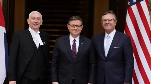 Reuters Commons Speaker SIr Lindsay Hoyle, US House Speaker Mike Johnson and US Ambassador to the UK Warren Stephens pose during a visit to the House of Commons. The three are dressed formally, posing in front of a union jack and a US flag.