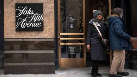 Getty Images Two people wearing winter clothing leave a Saks Fifth Avenue store.