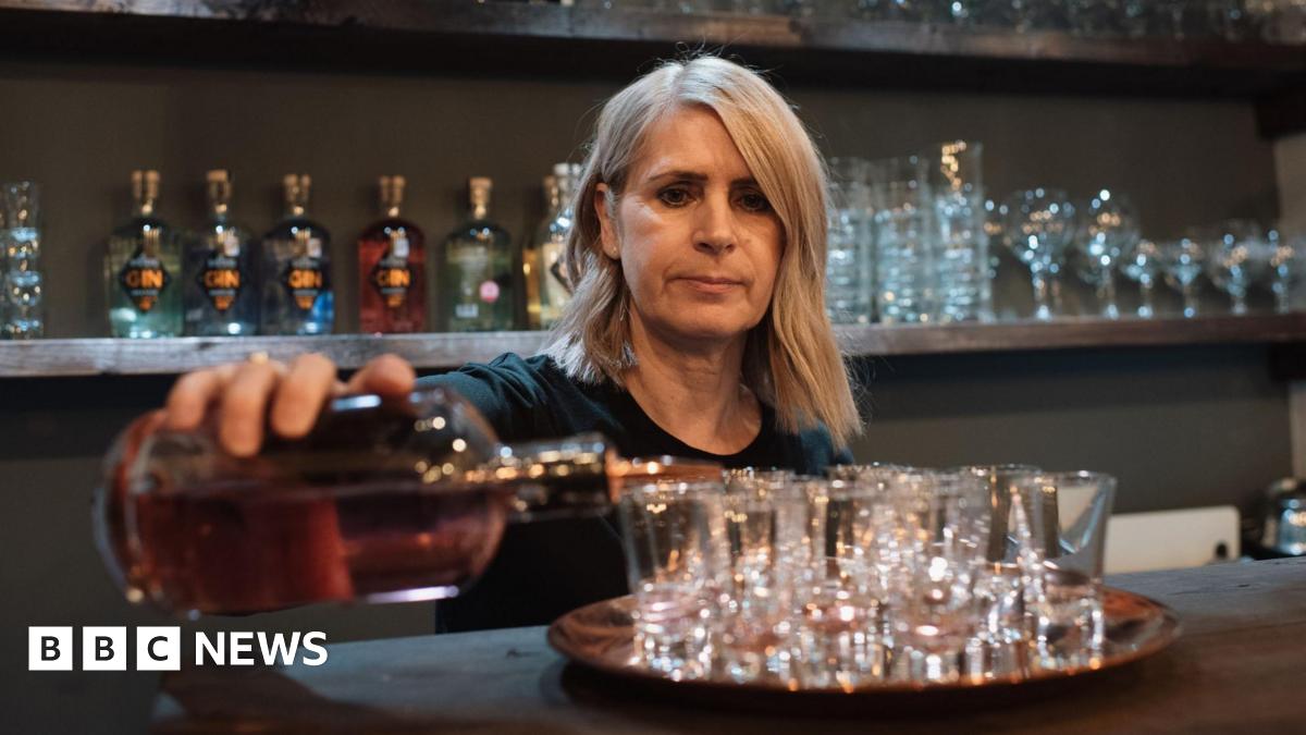 Woman working in bar pour alcohol into shot glasses