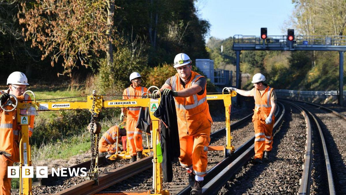 Five contractors wearing orange hi-vis clothing carrying out maintenance work on a railway line.