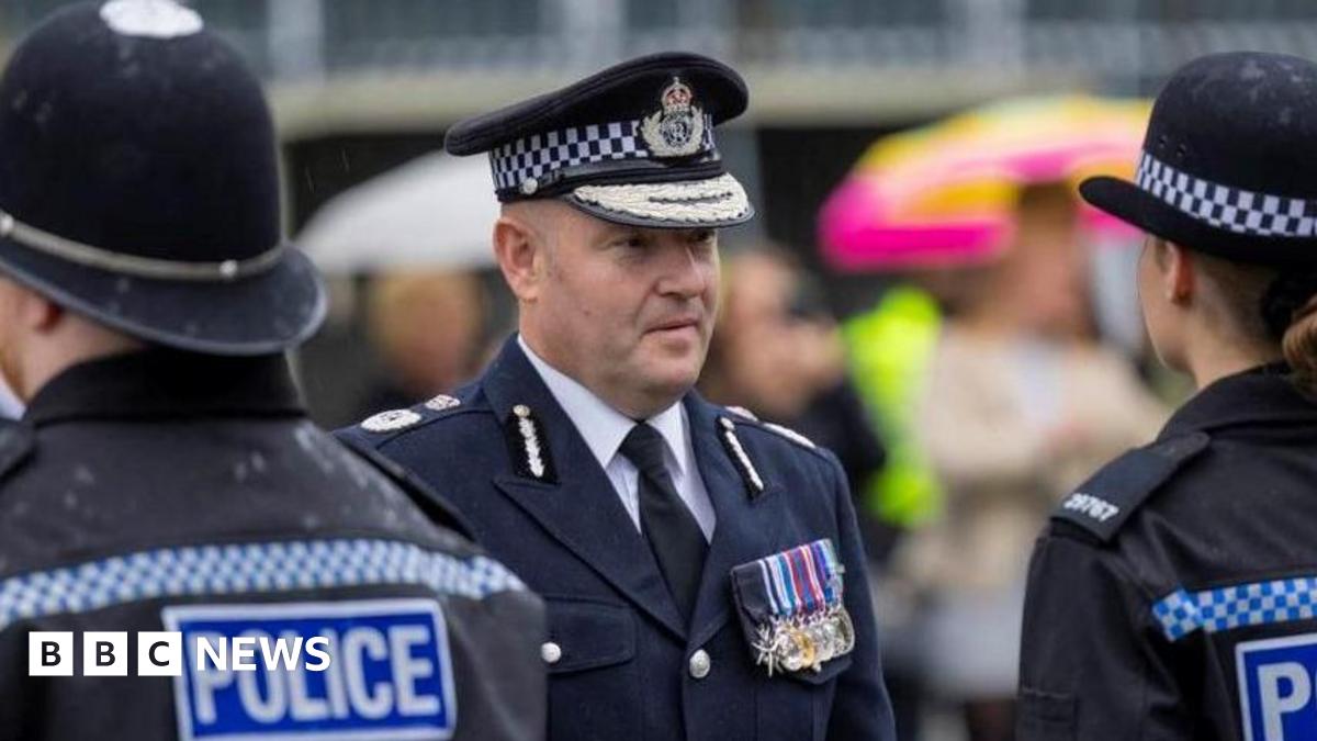 Craig Guildford looks at a line-up of police officers while dressed in full police uniform.