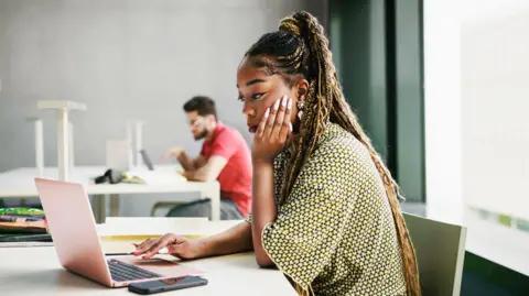 Getty Images A woman with brown hair and a green top sat staring at a laptop