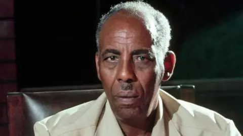 Corbis/Getty Images Siad Barre in a safari suit staring at the camera.