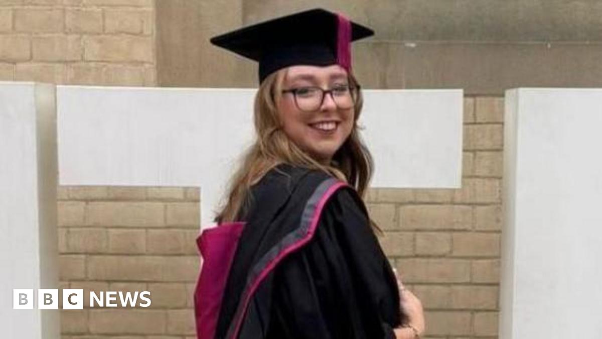 Stephanie Irons wearing a graduation gown and cap in front of a sign for Nottingham Trent University