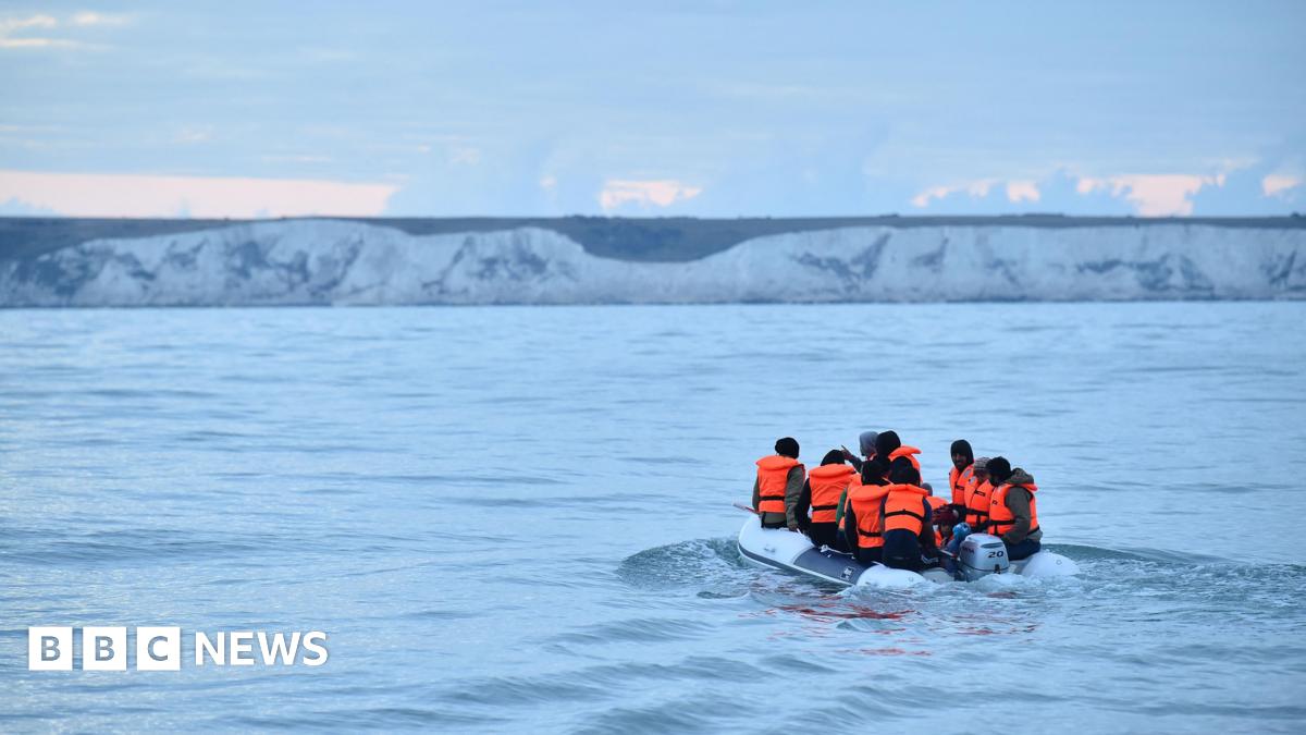 People in orange life-jackets on a small boat heading towards white cliffs that are in the background