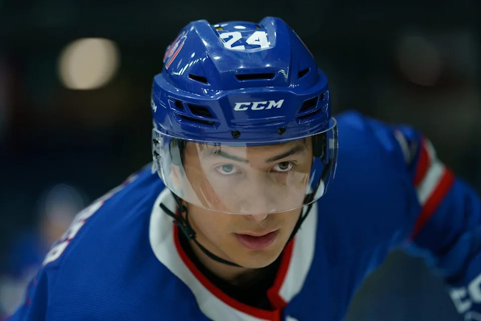 A close-up of the face of an Asian man in a hockey helmet and uniform
