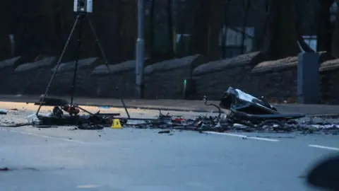 Phil Taylor Crash scene has debris strewn across the road. A yellow number marker is visible.