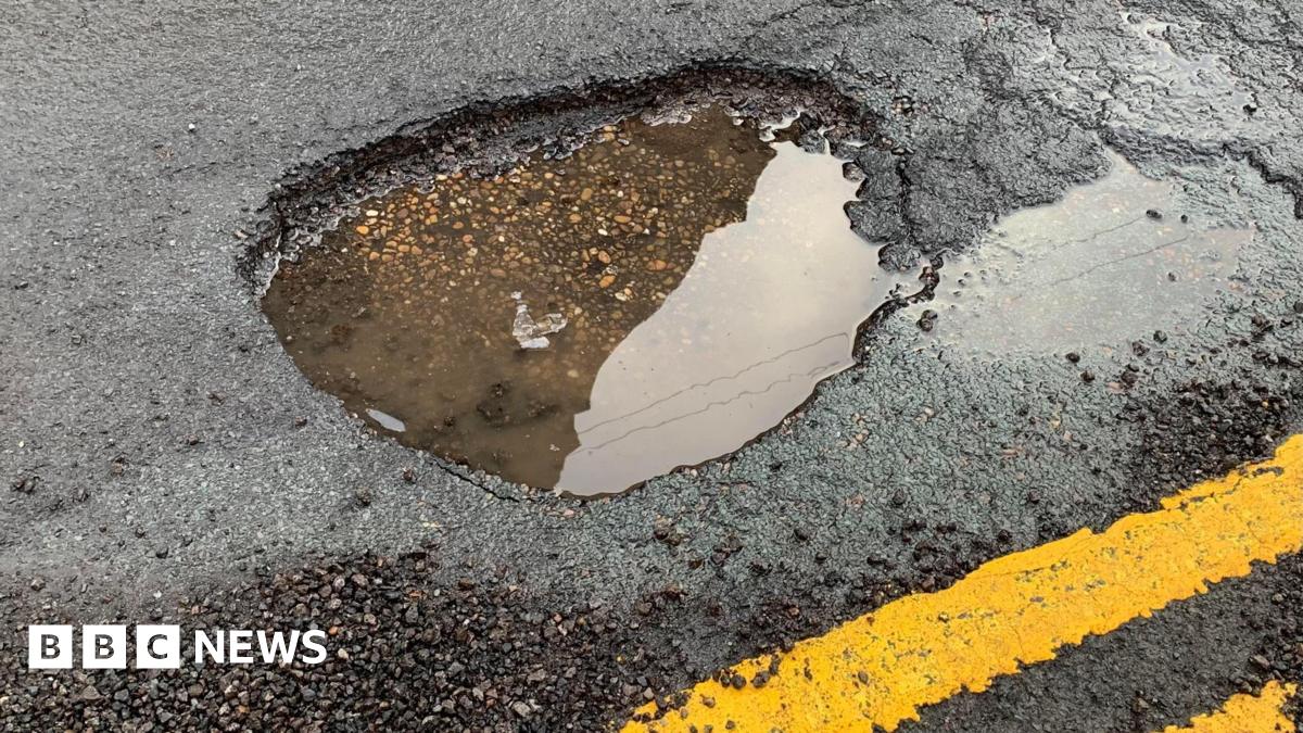 A pot hole on a road is filled with water and next to a double yellow line
